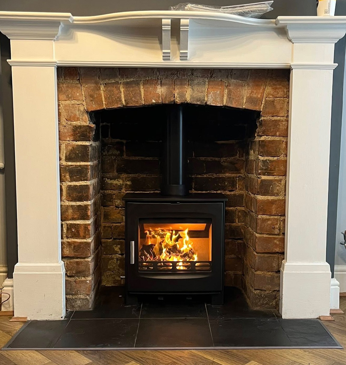 Exposed brick fireplace with an ornate white mantel and a black log stove